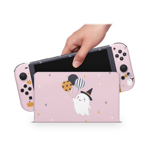 A hand is holding a Nintendo Switch console with a pink and black design featuring a ghost and balloons.