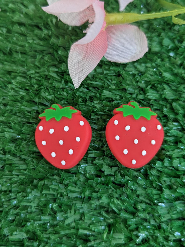 two red plastic strawberries with white polka dots placed on a green surface.