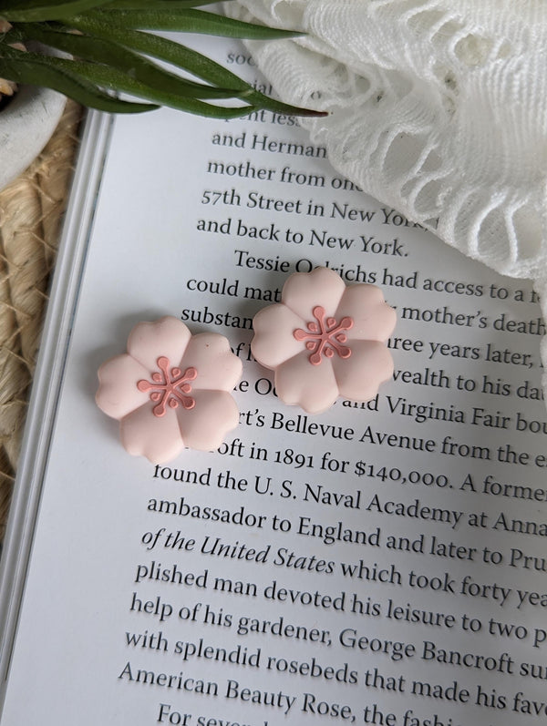a close-up view of a book with pink flower-shaped earrings resting on the pages.