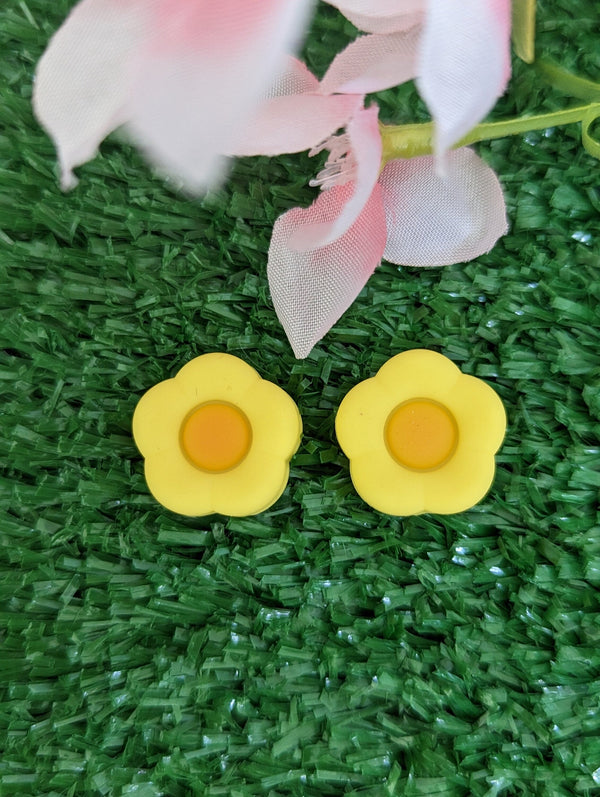 two yellow flower-shaped objects placed on a green surface, with a pink flower in the background.