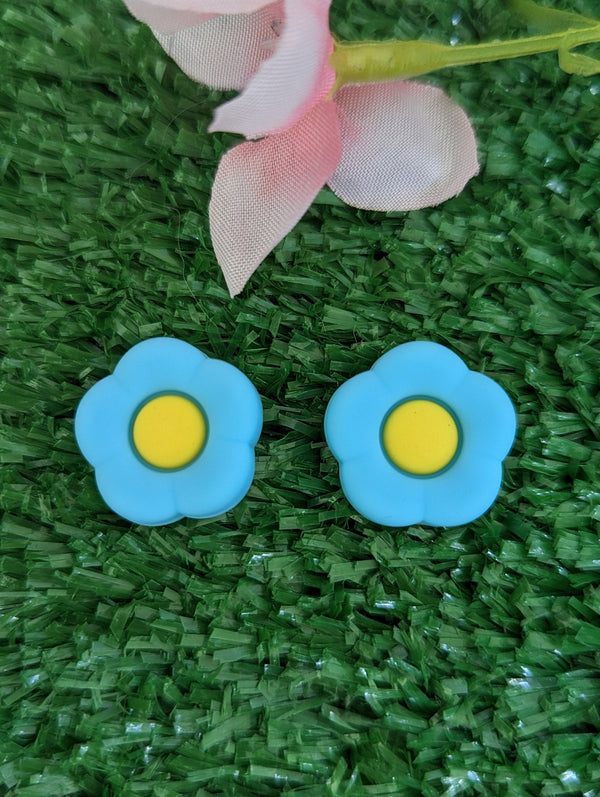two blue flower-shaped earrings with yellow centers, placed on a green grass surface.