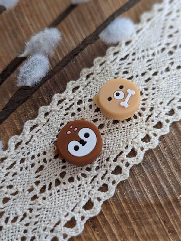 two cute animal-shaped buttons, one brown and one tan, placed on a white lace doily.