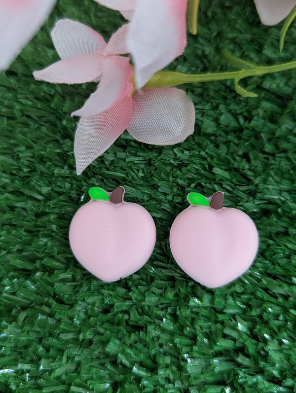 two pink heart-shaped objects with green leaves, placed on a green surface with a pink flower in the background.