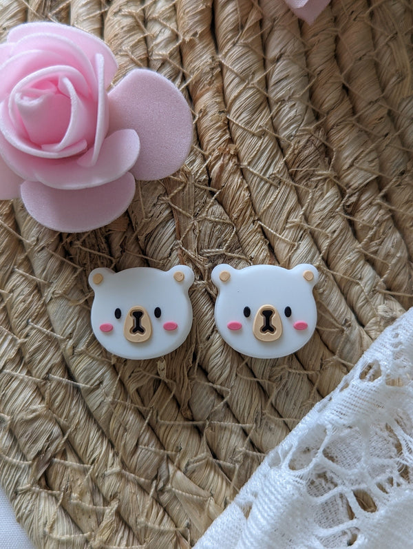 two cute white bear-shaped earrings with pink accents, placed on a woven straw background.