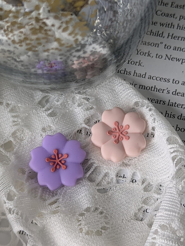 two flower-shaped objects, one purple and one pink, placed on a white lace surface.