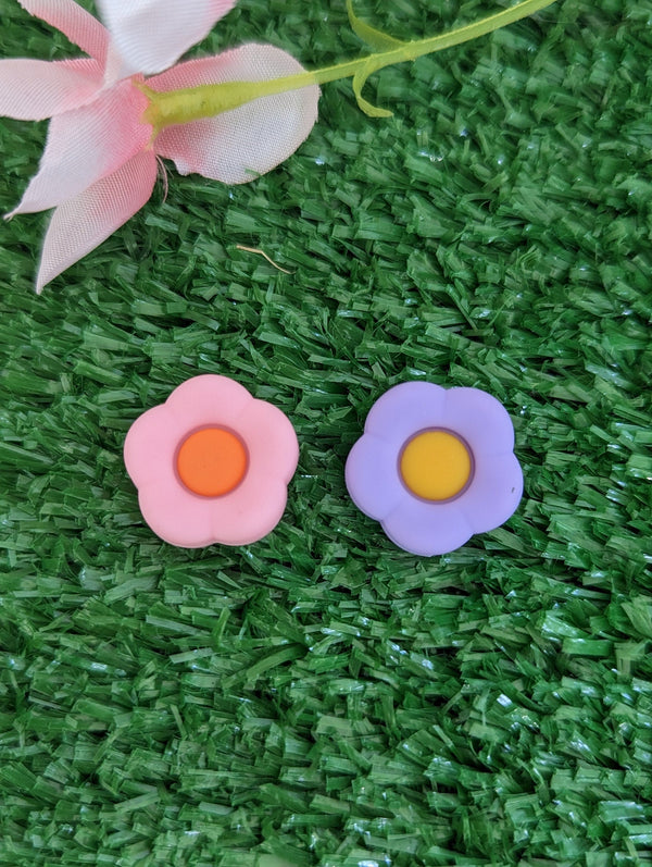 two flower-shaped objects, one pink and one purple, resting on a green surface.