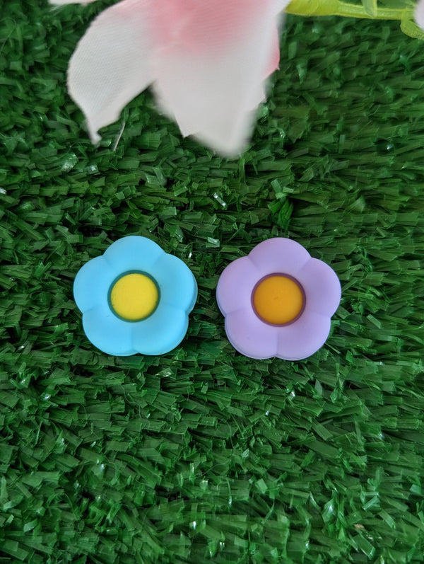 Two flower-shaped objects, one blue and one purple, are placed on a green surface resembling grass or artificial turf.