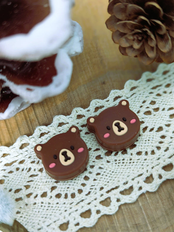 two chocolate bear-shaped cookies placed on a lace doily, with a pine cone and a mushroom in the background.