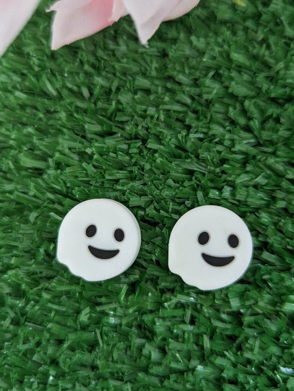 two white ghost-like objects with black eyes and smiling mouths, placed on a green surface.
